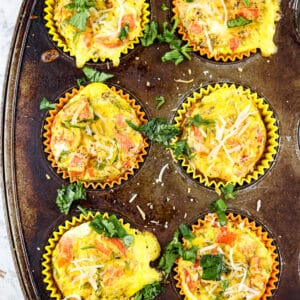 Old rusted muffin tin with 6 veggie and egg frittatas pictured on white marble background.