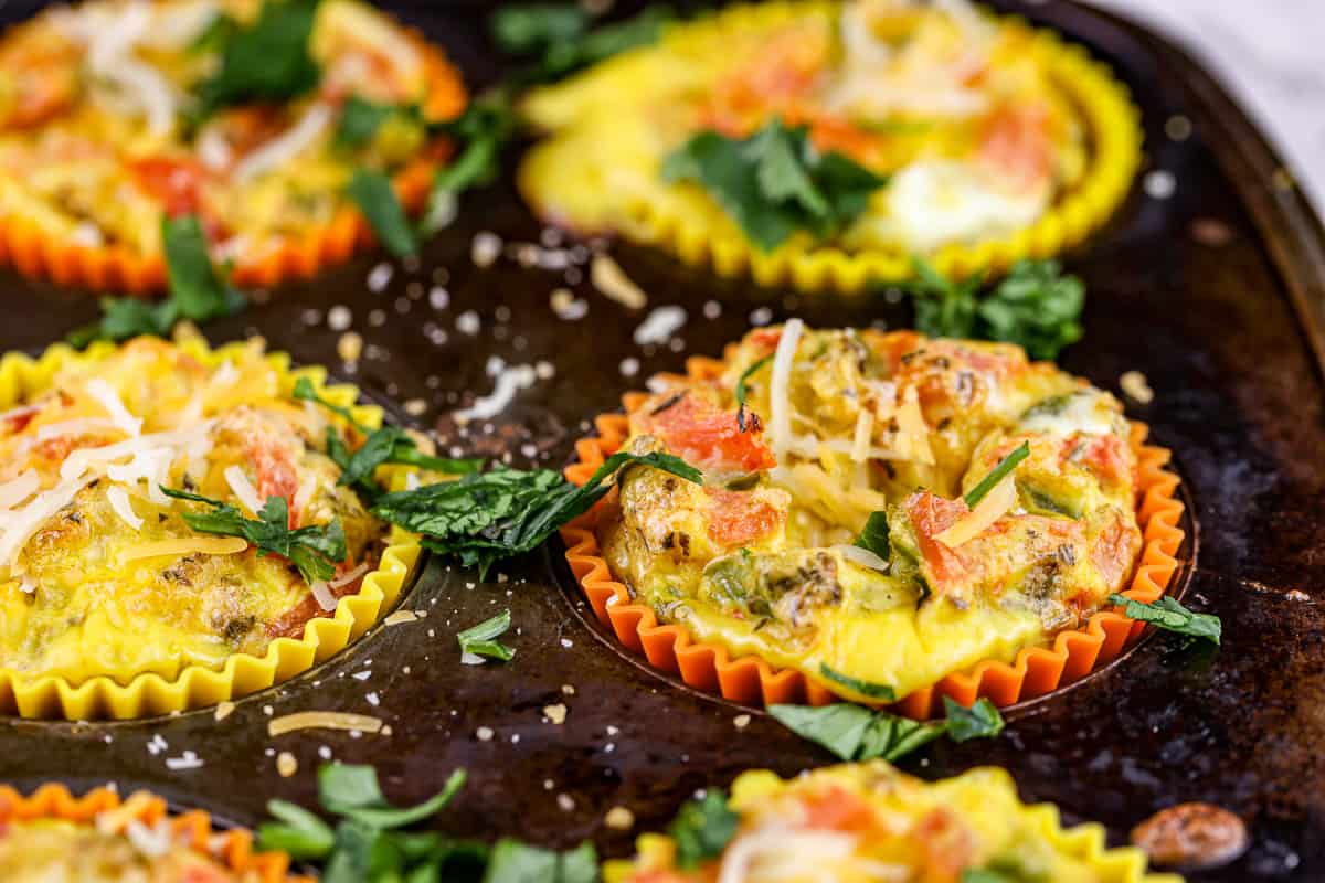 Close up shot of egg frittatas with veggies and cheese on top in a rusted muffin tin.