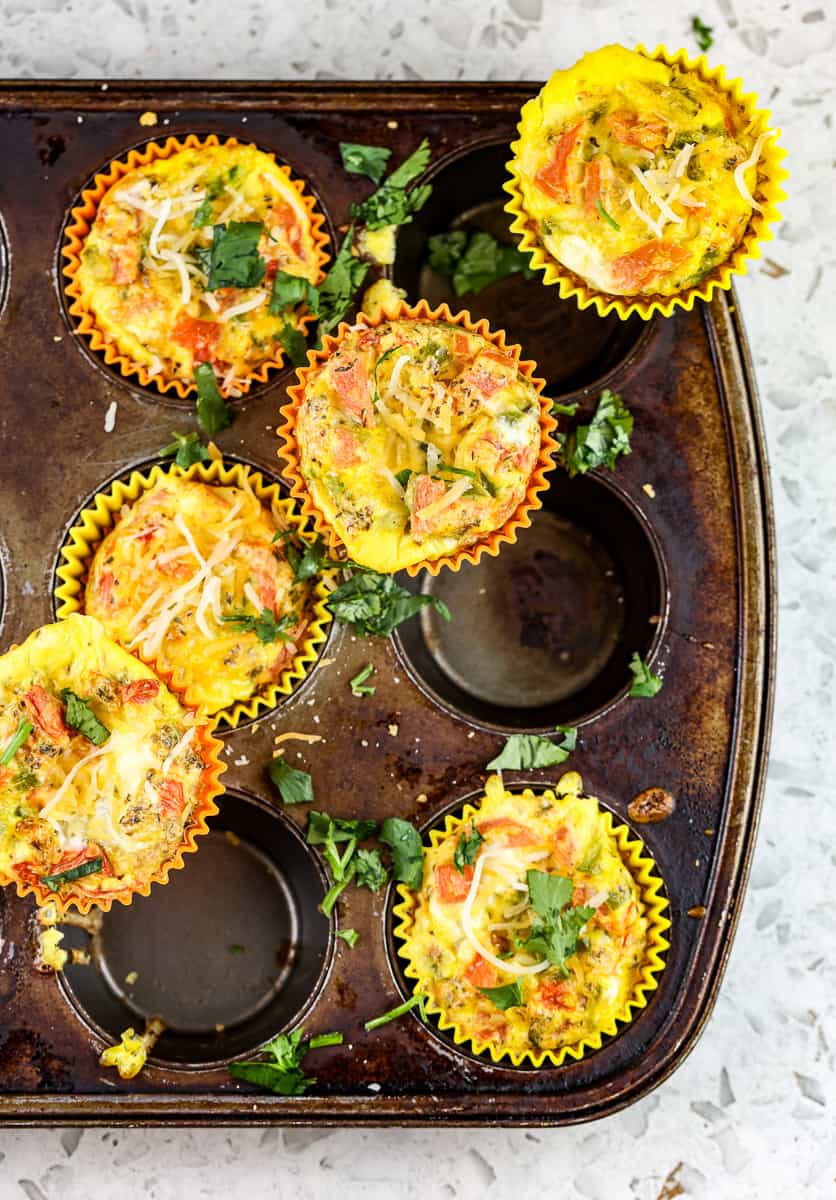 Yellow veggie egg frittatas on rusted muffin tin against a white backdrop.