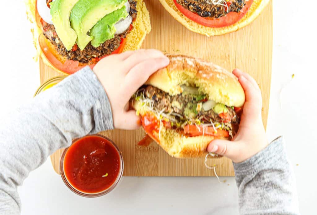 Toddler hands picking up a black bean burger to eat.