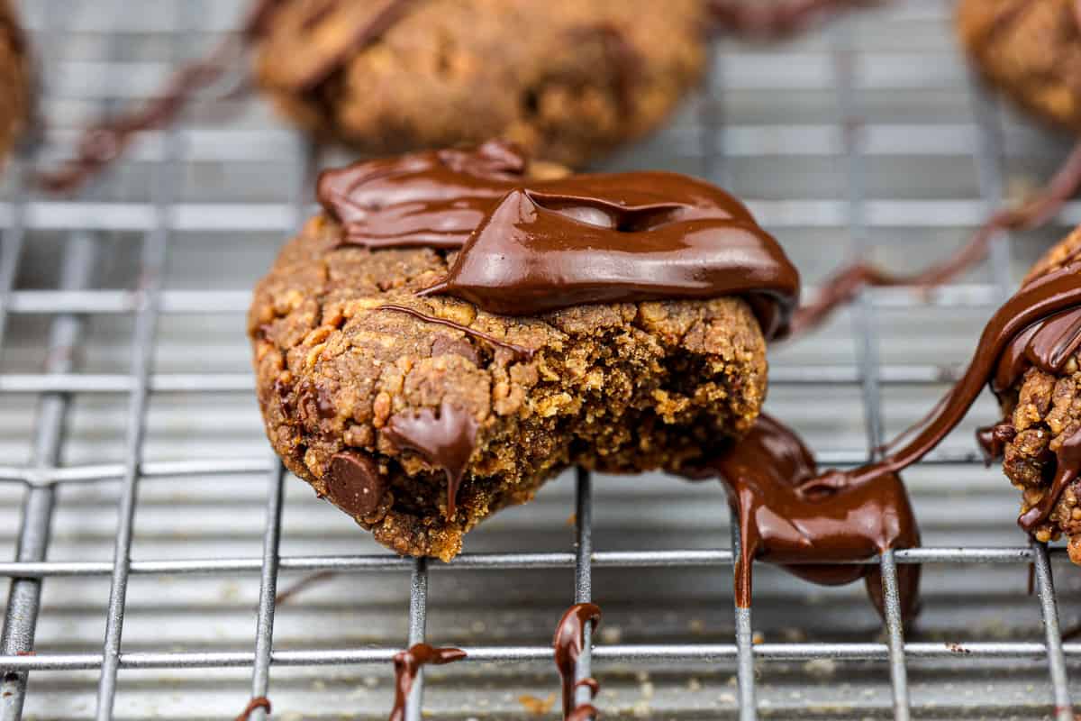 Cookie with chocolate drizzle on silver baking sheet with a bite out of it.