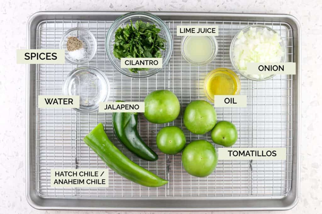 Silver baking sheet with green peppers, tomatoes, spices, and onion on top to make salsa verde.