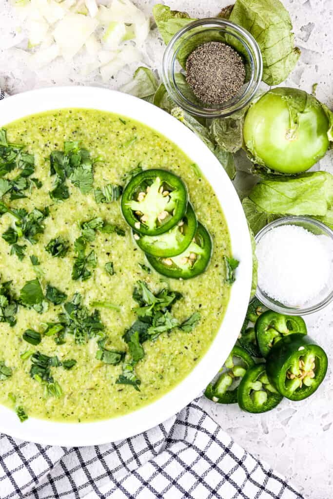 White bowl filled with hatch chile salsa verde topped with cilantro and jalapenos slices on a white backdrop.