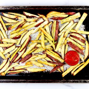 Image of French fries on a baking sheet with ketchup.