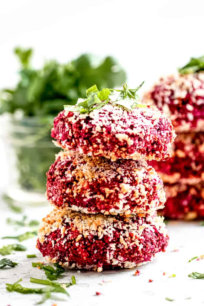 Three stacked beetroot burgers on white backdrop.