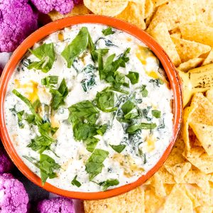 Image of plated spinach dip with chips and cauliflower around it.