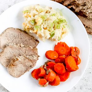 White plate with round roast, carrots and mashed potatoes.