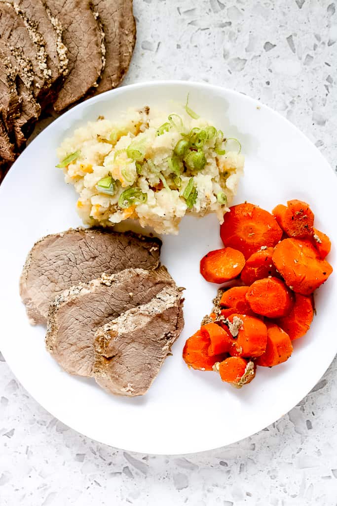 Long image of dinner plate with round roast, carrots and mashed potatoes.