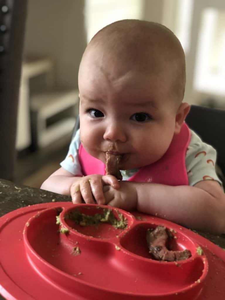 Image of baby eating beef steak strip as first food for baby led weaning.