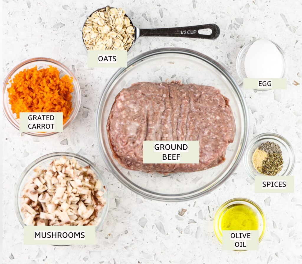 White tile with glass bowls filled with baby meatballs ingredients, including raw ground beef, mushrooms, carrots, oil and spices.