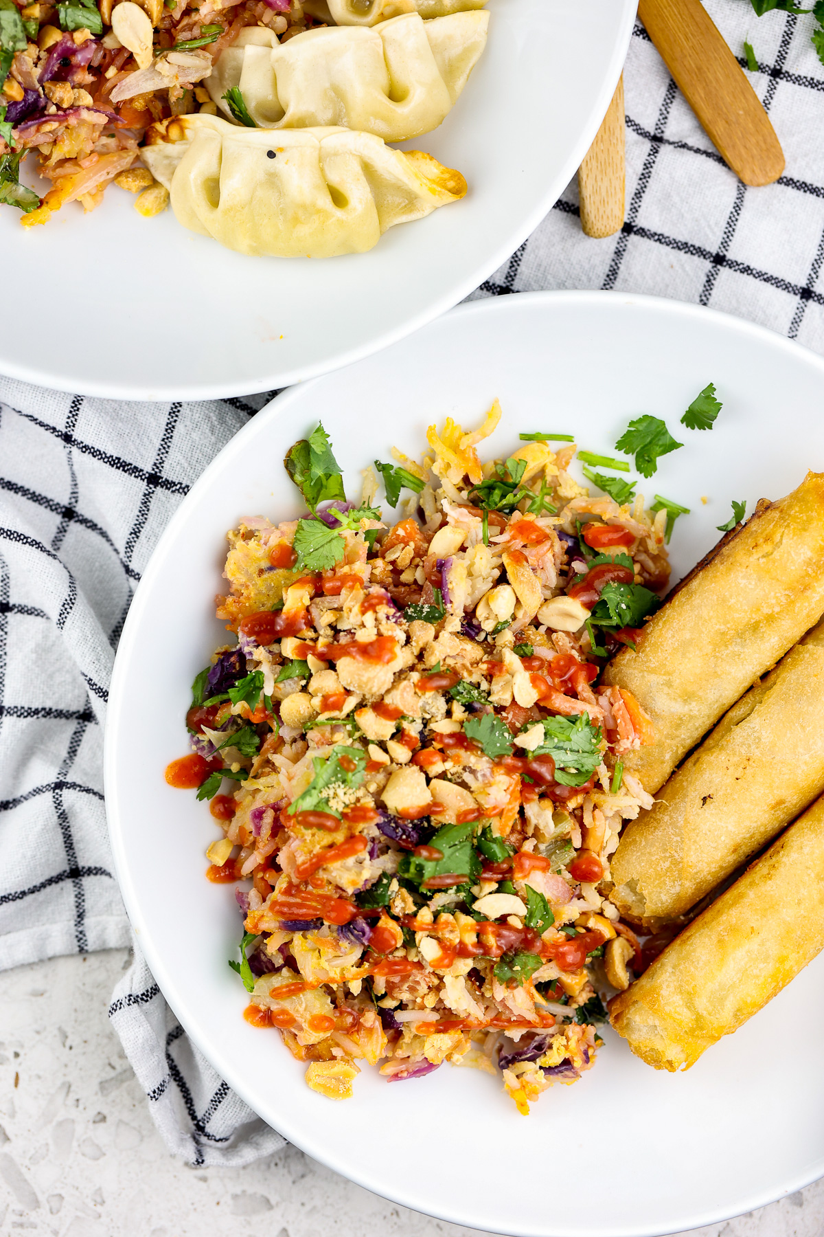 Picture of white rimmed bowl with veggies and fried rice with 3 egg rolls on the side and red sauce drizzled over the top.
