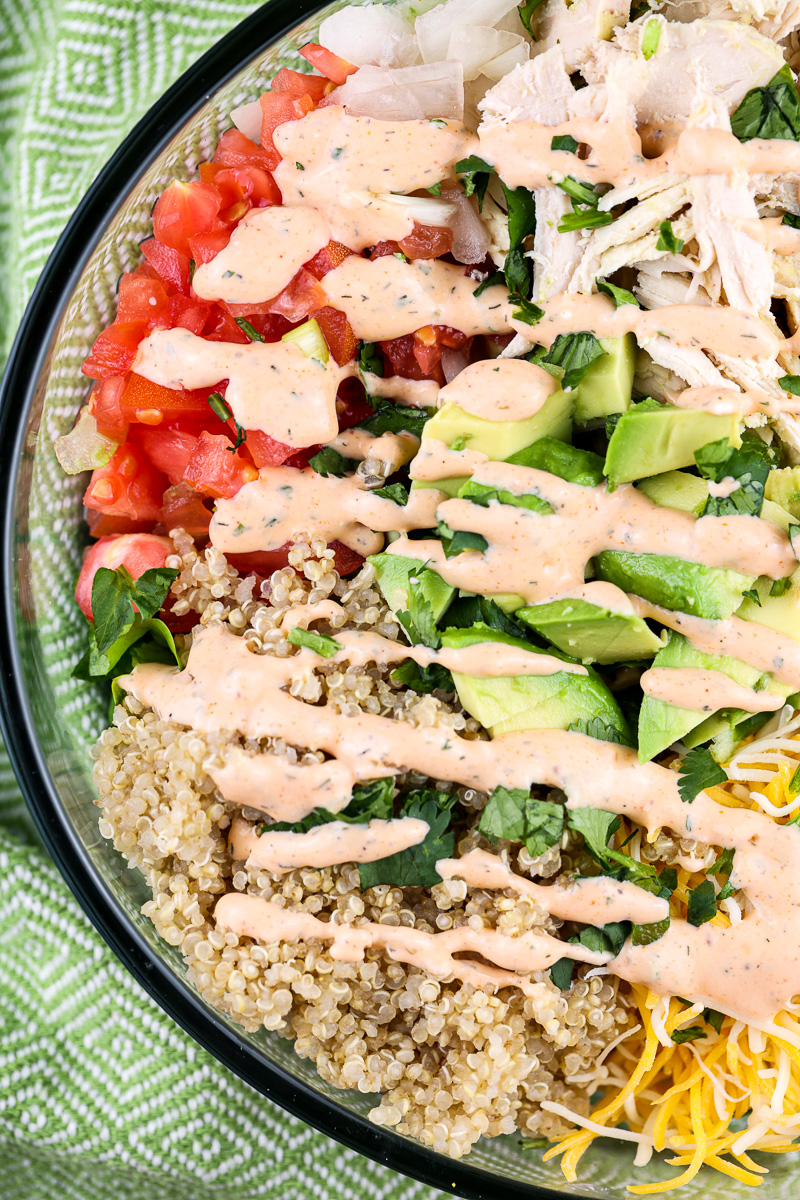 Green napkin with a glass bowl filled with veggies, chicken and tossed in red buffalo dressing.