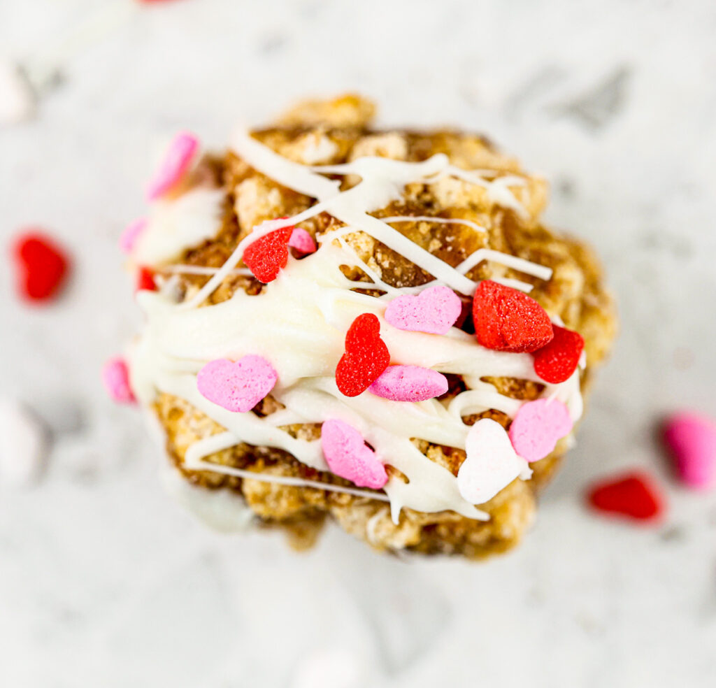 White marble tile with brown cereal cake pop with white drizzle icing and red and pink heart sprinkles on top.