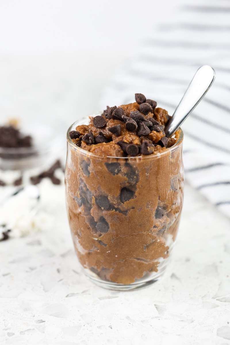 White marble backdrop with single glass jar filled with chocolate cookie dough and mini chocolate chips on top with a tiny spoon sticking out.