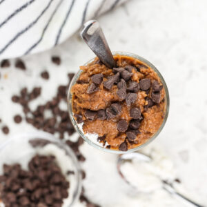 White marble backdrop with single glass jar filled with chocolate cookie dough and mini chocolate chips on top with a tiny spoon sticking out.