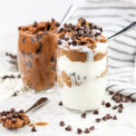 White tile with two glasses filled with white ice cream and stuffed with vegan chickpea chocolate chip cookie dough.