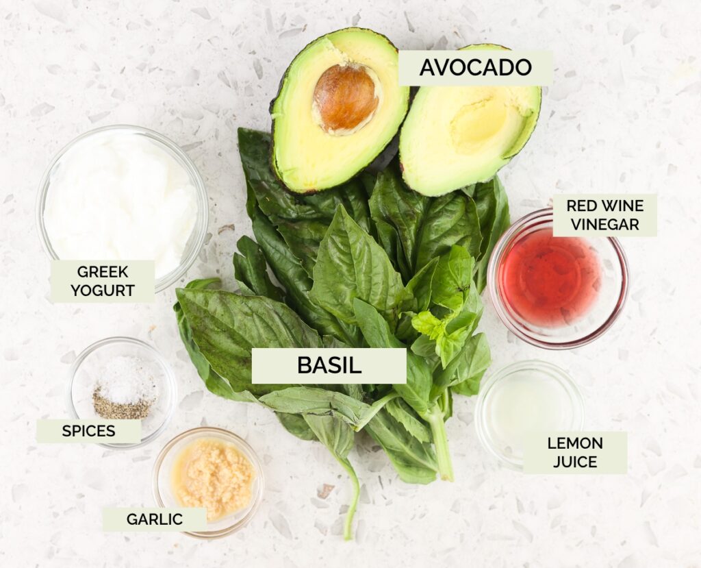 White tile backdrop with fresh green basil, avocado, and spices on top to make Avocado Pesto Pasta.