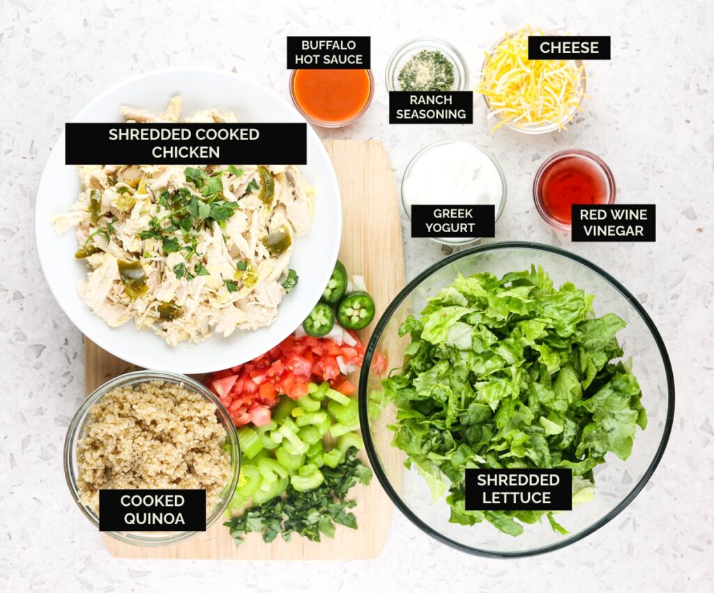 White tile with bowls of shredded chicken, lettuce, veggies, and sauces to make Buffalo Chicken Grain Bowls.