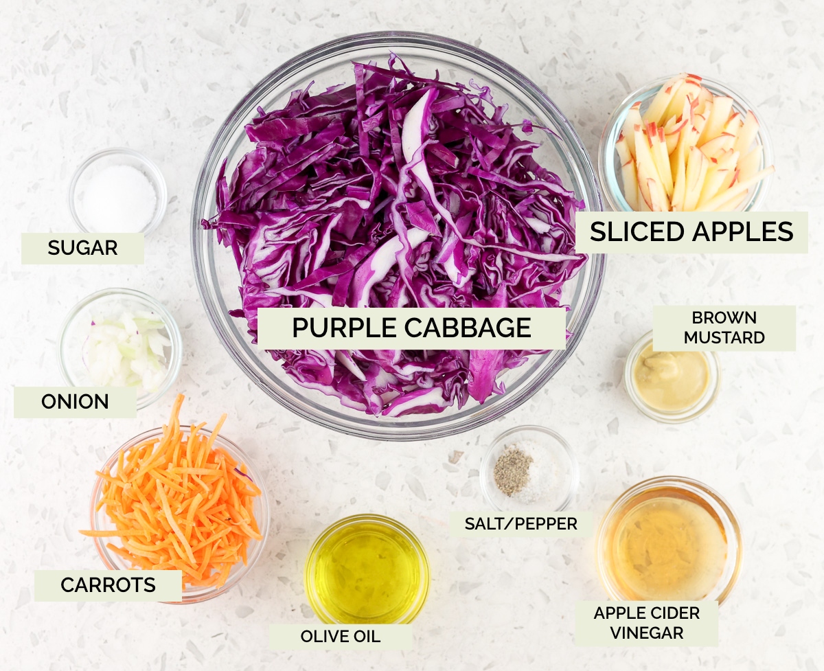 White marble backdrop with glass bowls filled with purple cabbage, vinegars, and carrots.