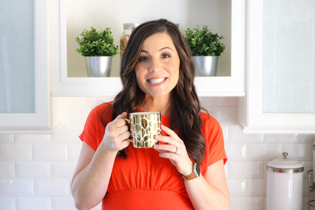 Headshot of Liz Shaw on About Me page holding a gold mug and wearing a red dress.