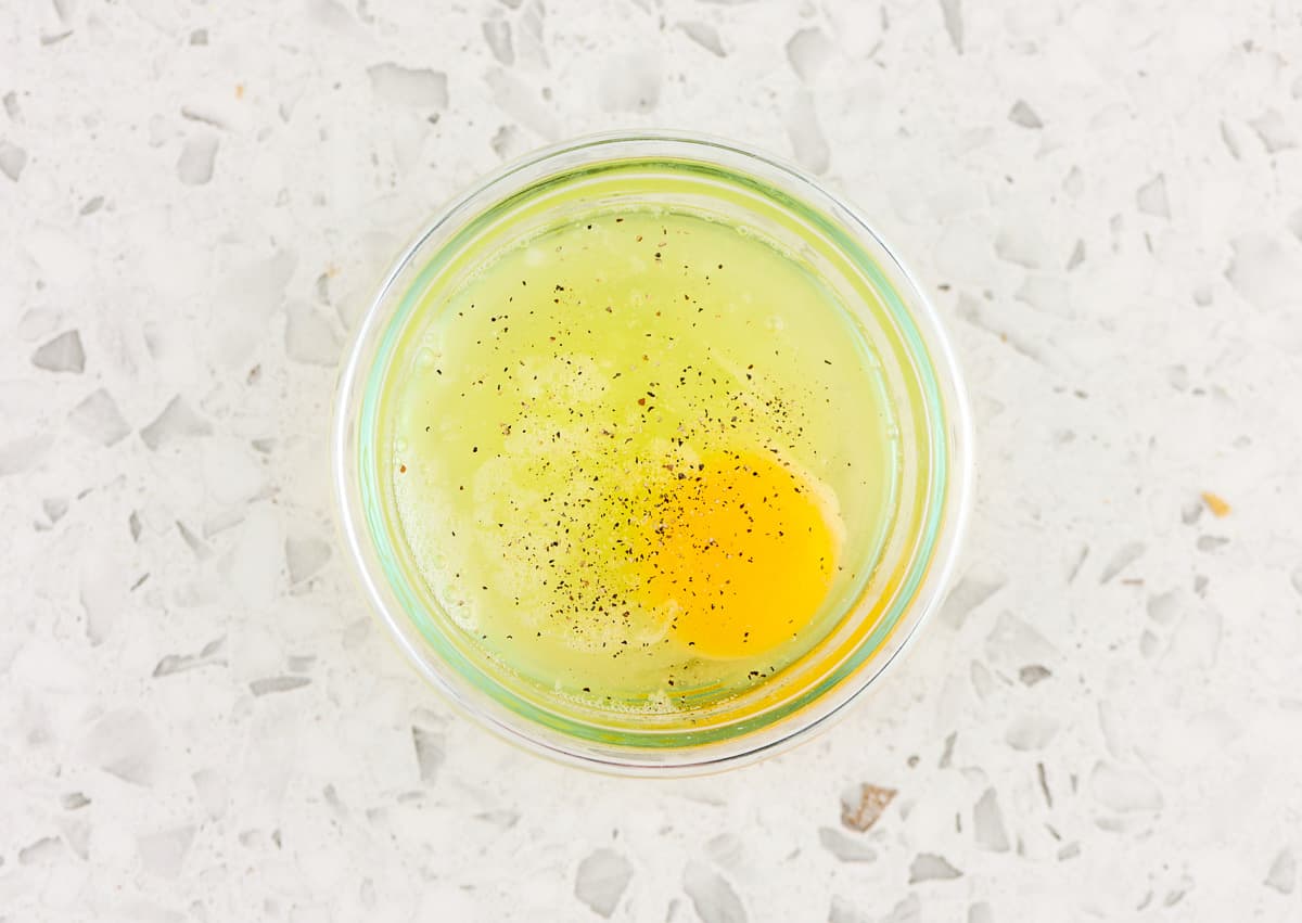 White marble backdrop with egg with yellow yolk in a glass bowl.