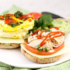 Egg McMuffin sandwich on whole grain bun with deli turkey, egg, and red sriracha sauce on top.