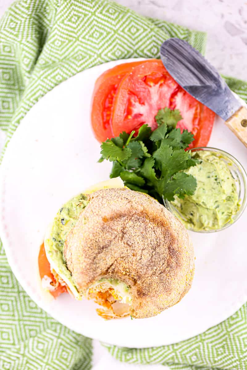 Green napkin underneath white plate with brown English Muffin and tomato, pesto and cilantro garnish.