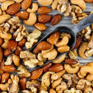 Silver baking sheet covered with roasted cashews, almonds and walnuts with a metal serving handle in the center.