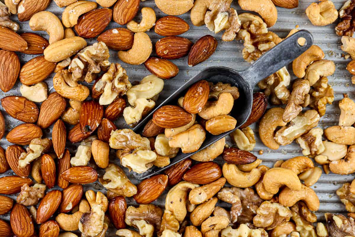 Silver baking sheet covered with roasted cashews, almonds and walnuts with a metal serving handle in the center. 