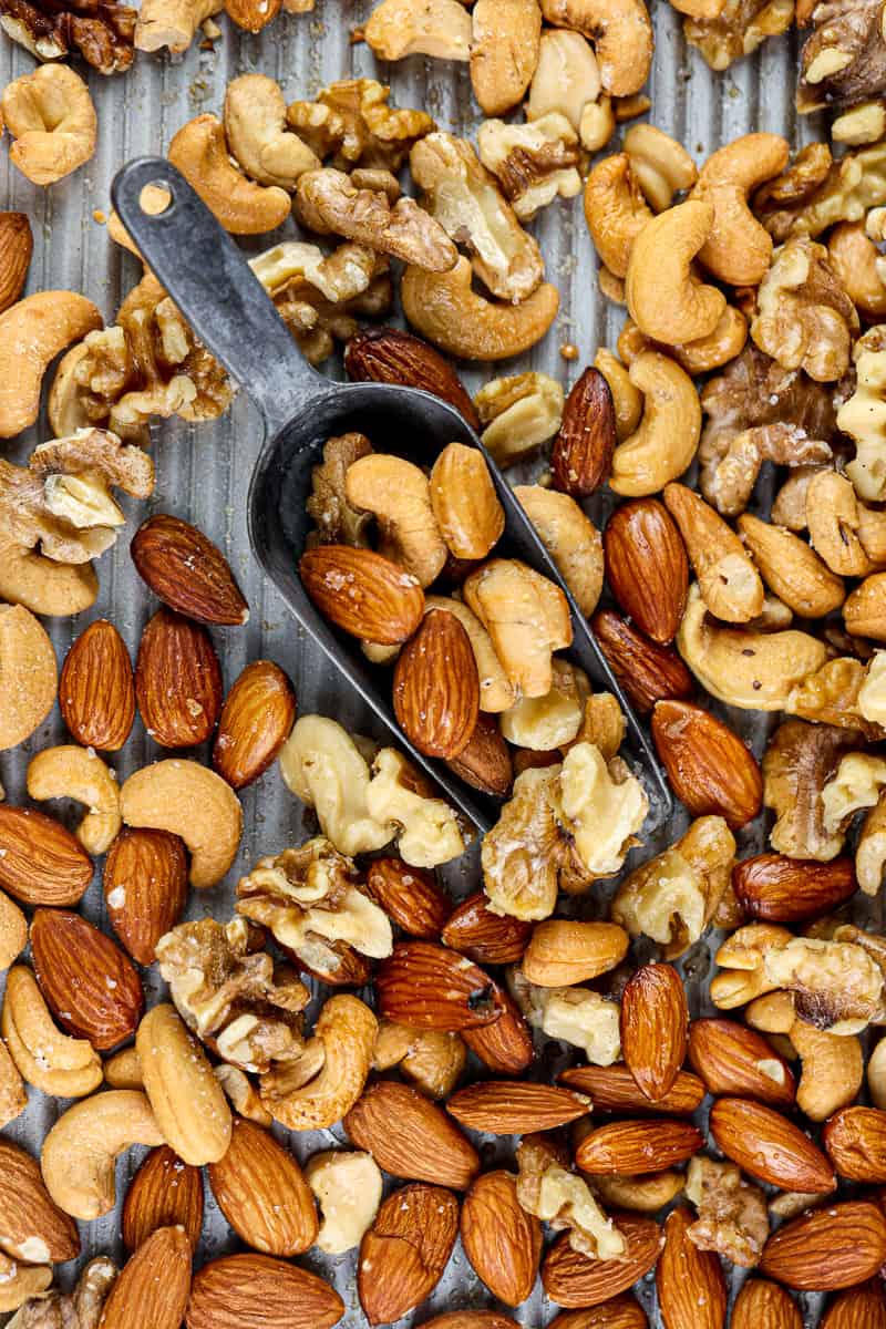 Silver baking sheet covered with roasted cashews, almonds and walnuts with a metal serving handle in the center.