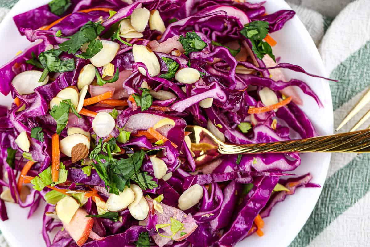 Close up picture of fork on purple cabbage slaw with sliced almonds and cilantro on top. 