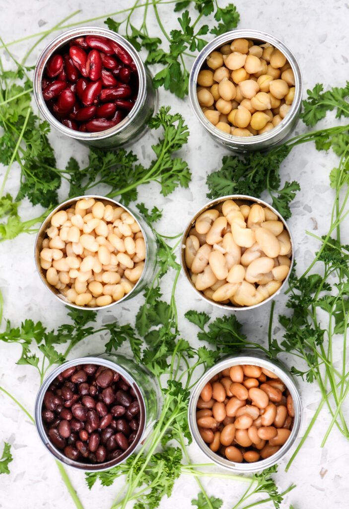 White marble backdrop with parsley leaves and opened canned beans in aluminum cans in a circle.