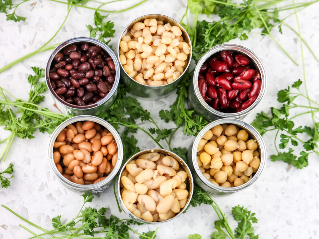 White marble backdrop with parsley leaves and opened canned beans in aluminum cans in a circle.