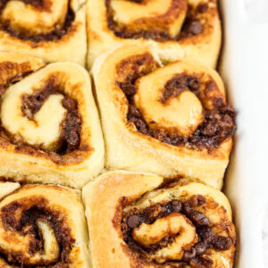 Brown Cinnamon Rolls in a white baking dish with a brown date filling peaking out.