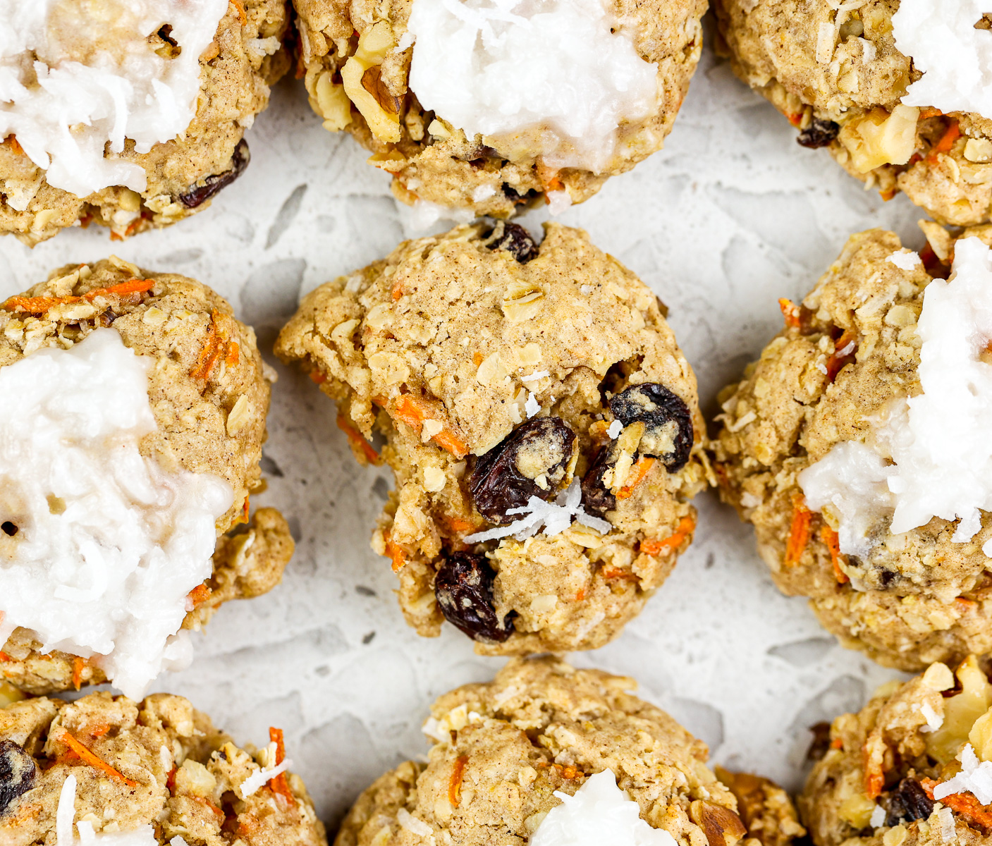 White marble backdrop with carrot cake cookies in rows and one in the center with a bite out of it.