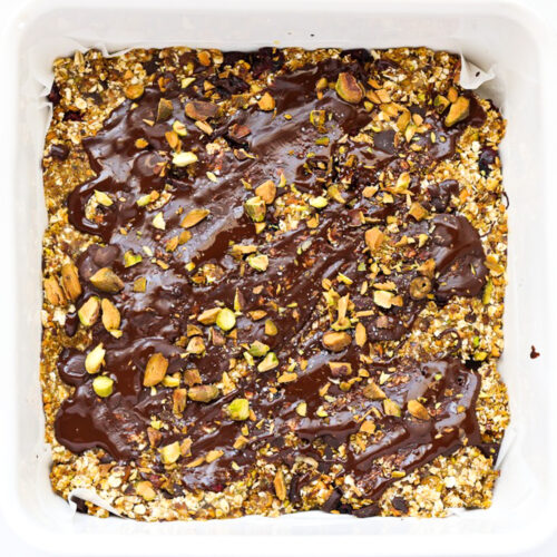 Chocolate covered no bake pistachio snack bars in white square container.