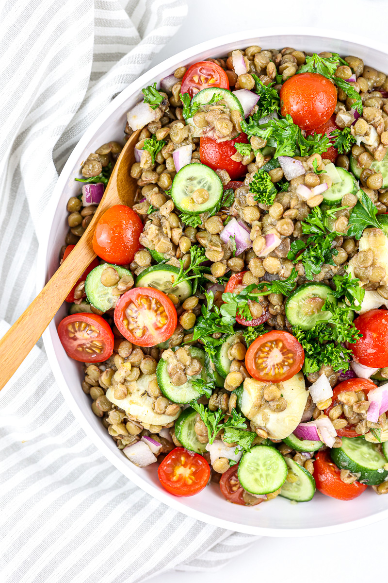 Large salad bowl with lentil salad against white backdrop with wooden spoon.