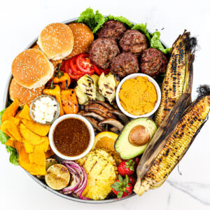 White marble backdrop with beef burgers and fixings on a board.