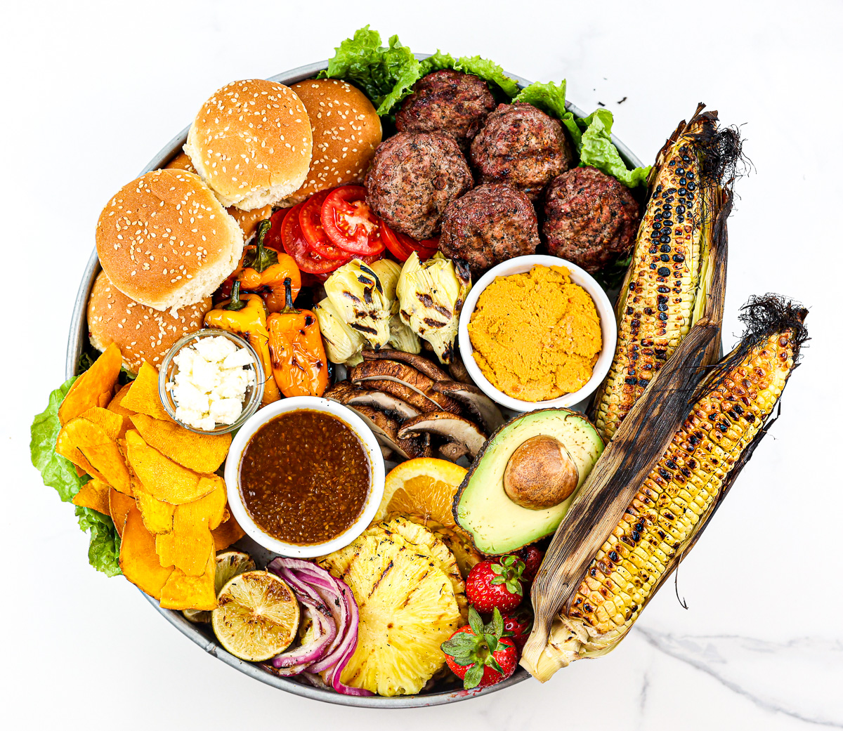 White marble backdrop with beef burgers and fixings on a board.