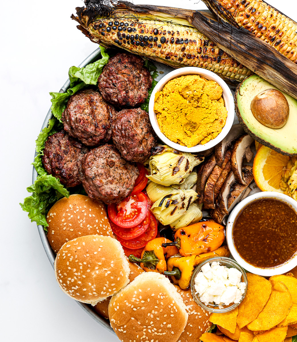 White marble backdrop with beef burgers and fixings on a board.