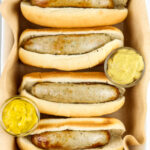 4 bratwursts in a white pan with mustard.