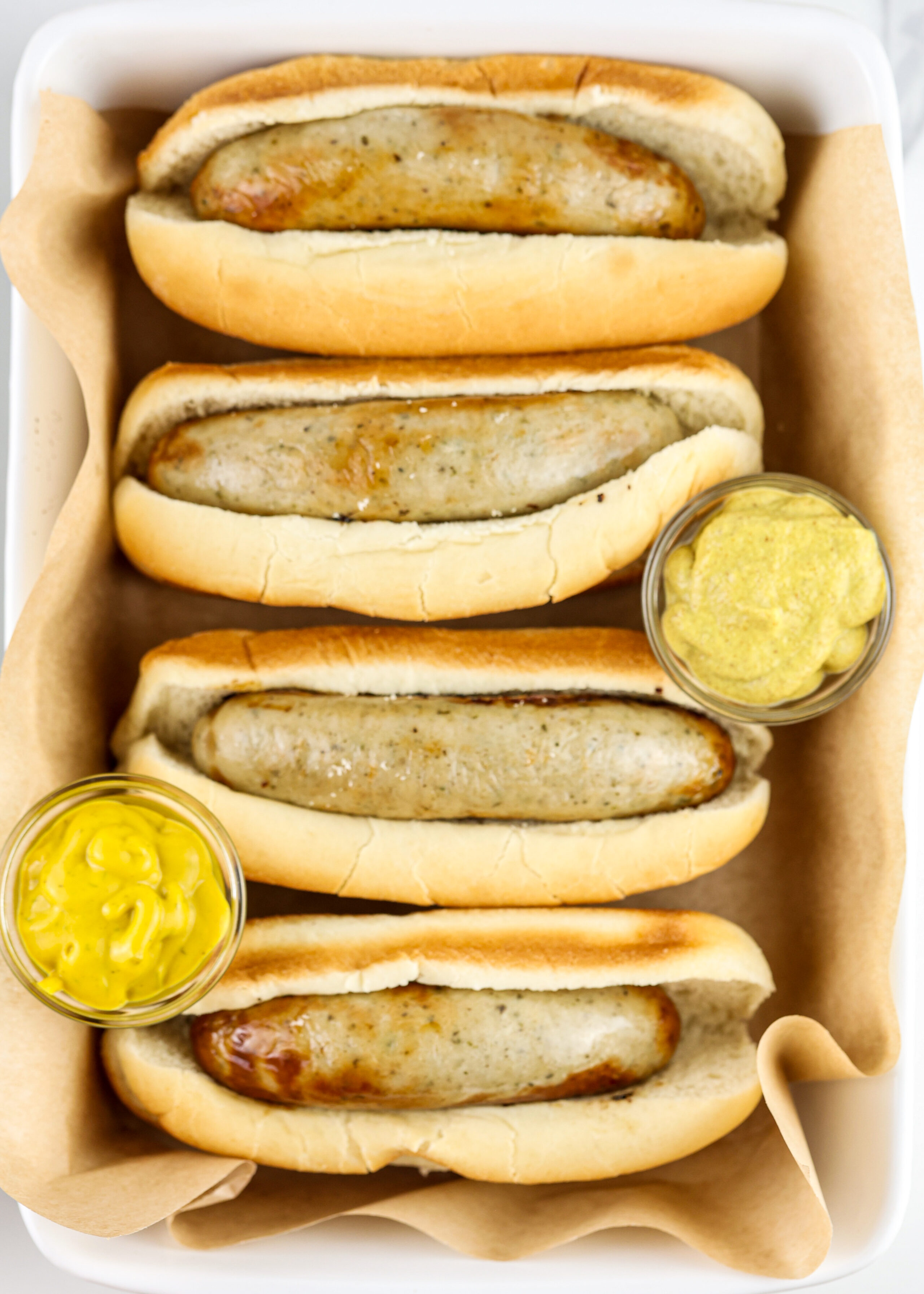 4 bratwursts in a white pan with mustard.