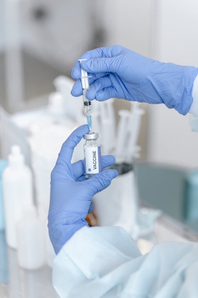 A picture of two gloved hands and a vile to dose out a vaccine.