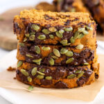 Three slices of pumpkin bread stacked on a piece of brown paper.