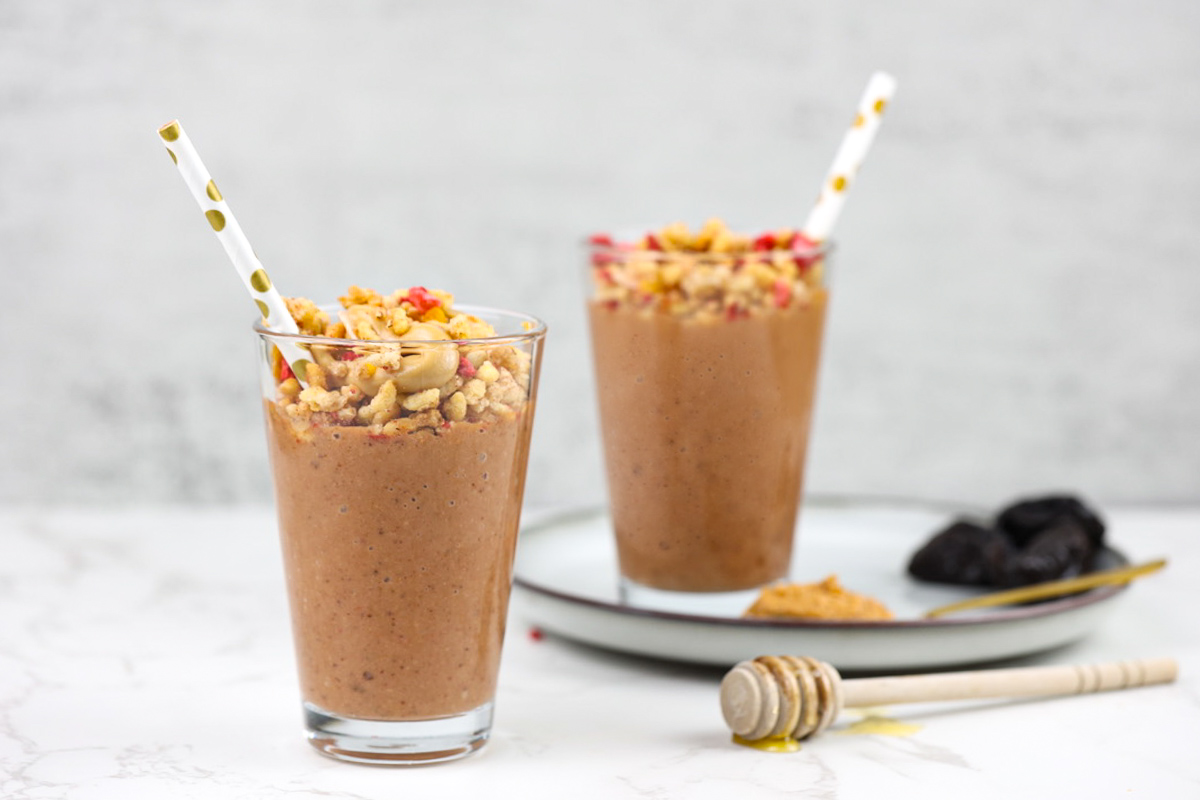 Two pb smoothie glasses with honey comb stick in backdrop.